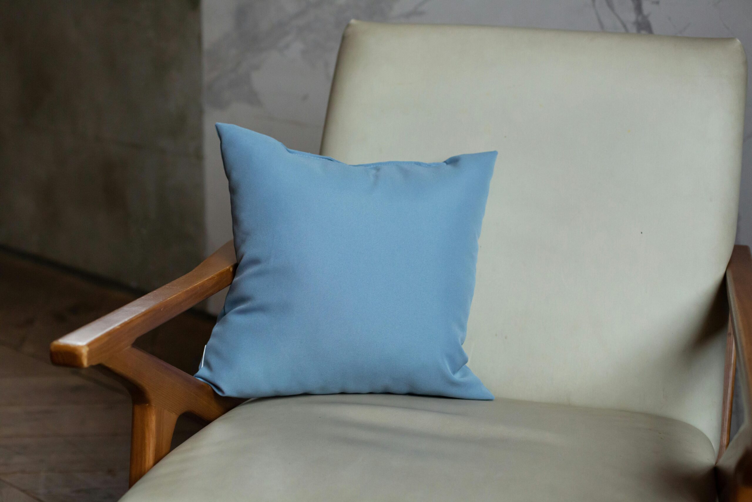 A stylish beige chair adorned with a soft blue throw pillow, conveying comfort and modern design.